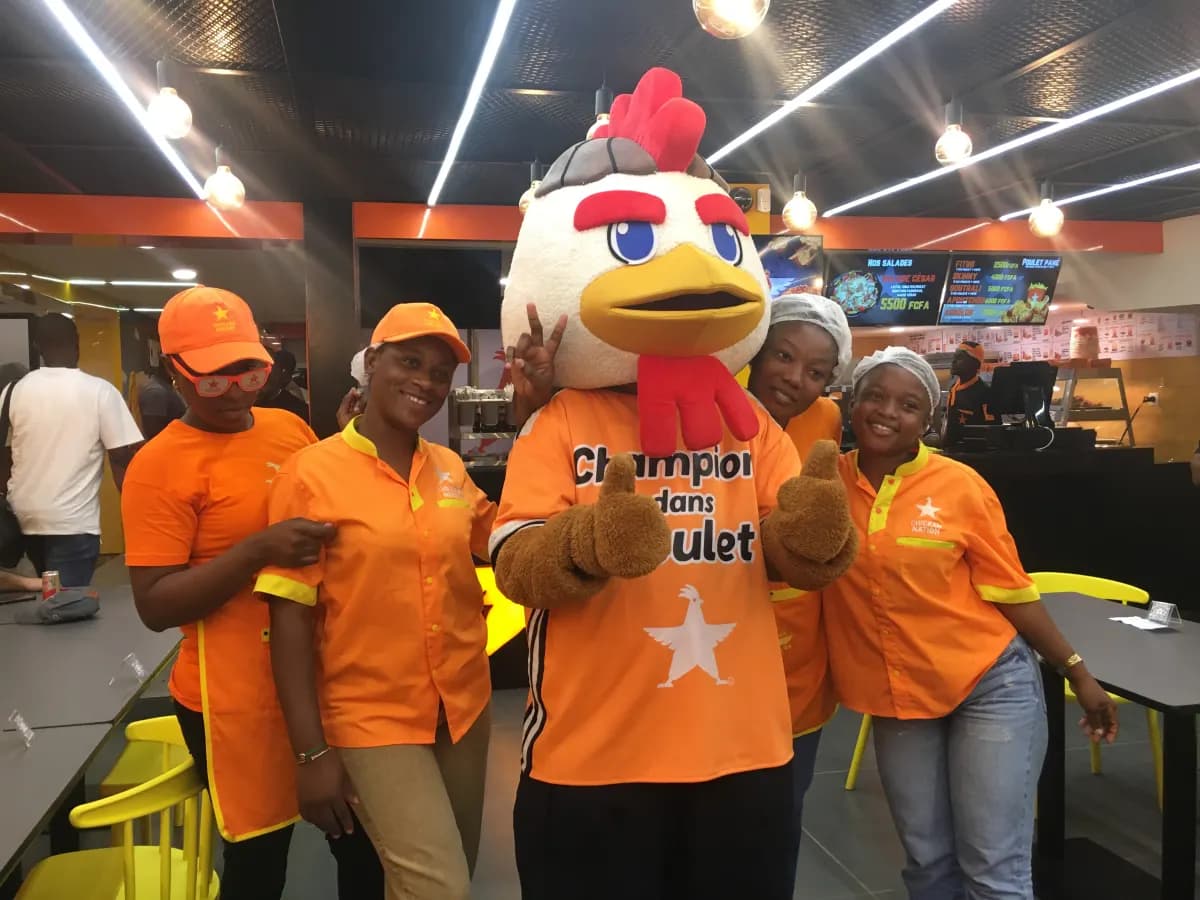 L'équipe Chicken Nation en tenue orange, avec la mascotte Champion dans poulet, dans un de nos restaurants